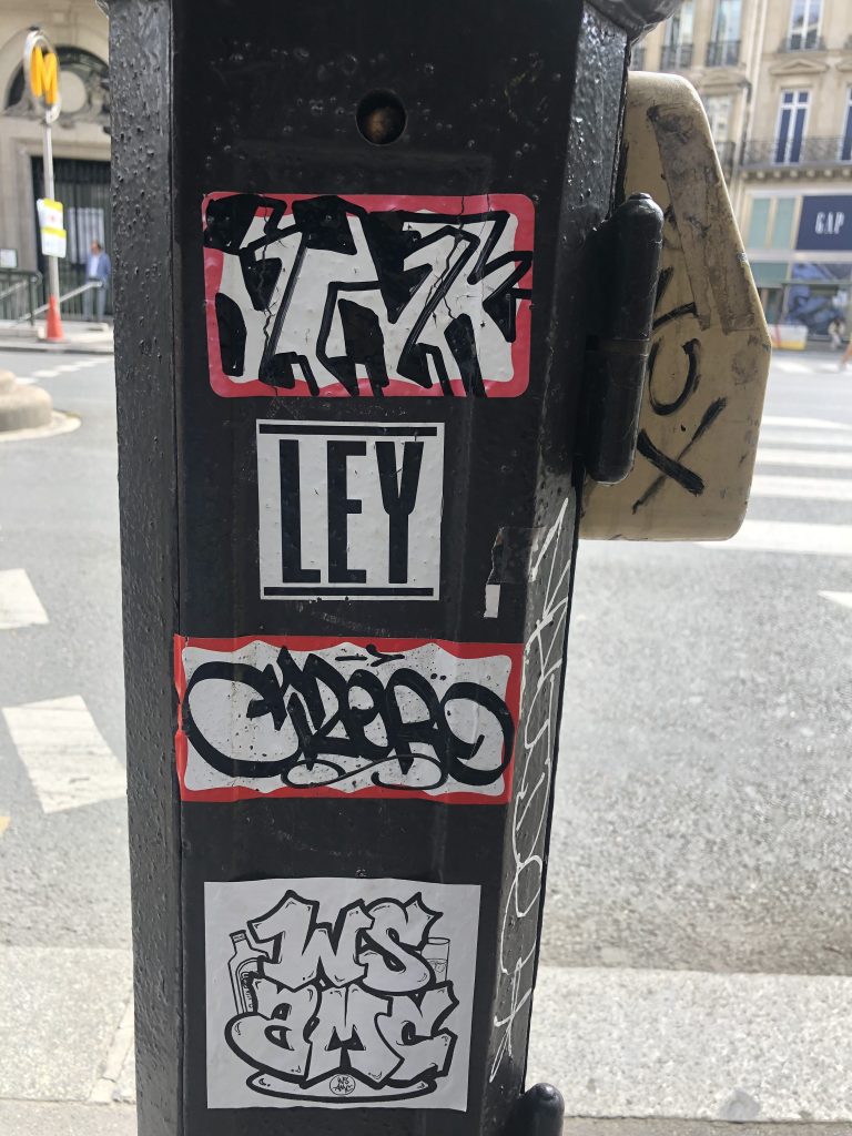 A crosswalk signal in Paris tagged with graffiti stickers